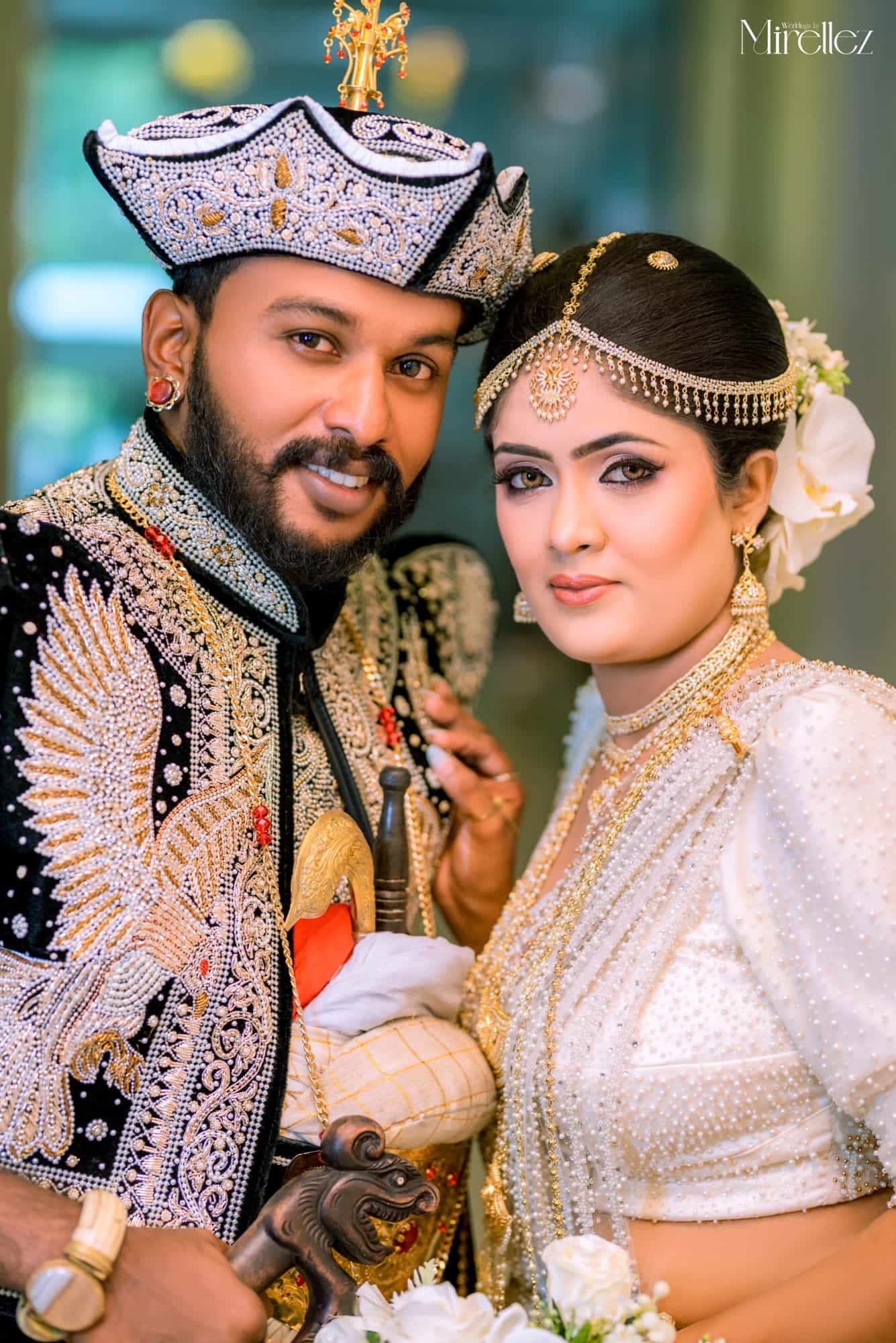 Close-up portrait of a Kandyan bride and groom, he in a jewelled nilame headdress, she in a white pearl osari with a gold headpiece