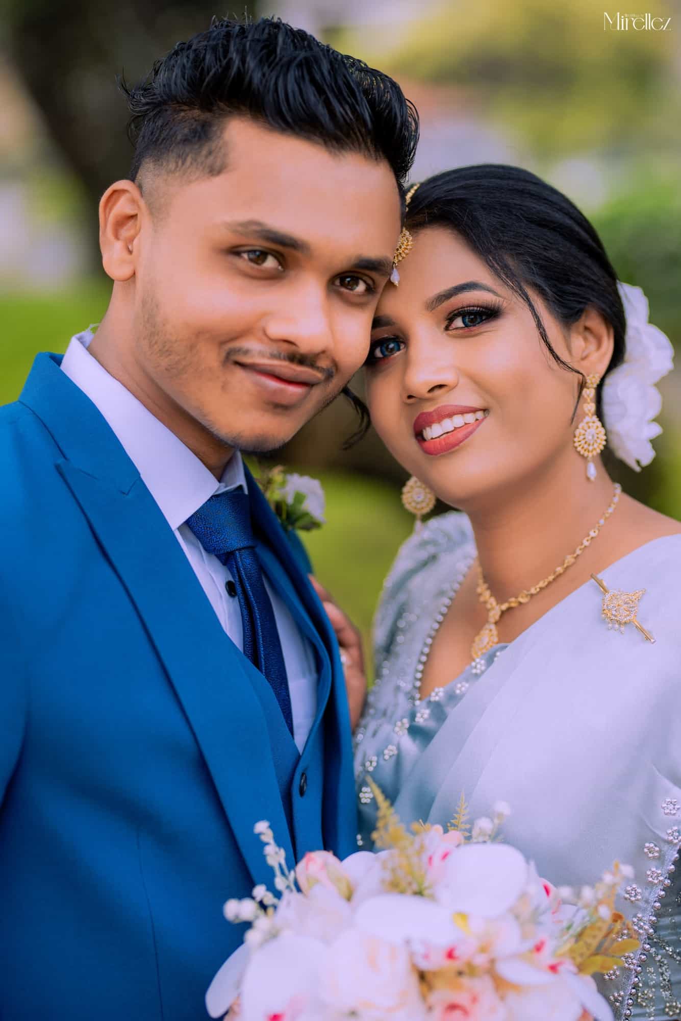 Dilshan and Dilshani cheek to cheek, he in a cobalt blue three-piece suit, she in a pale silver-grey saree with gold necklace