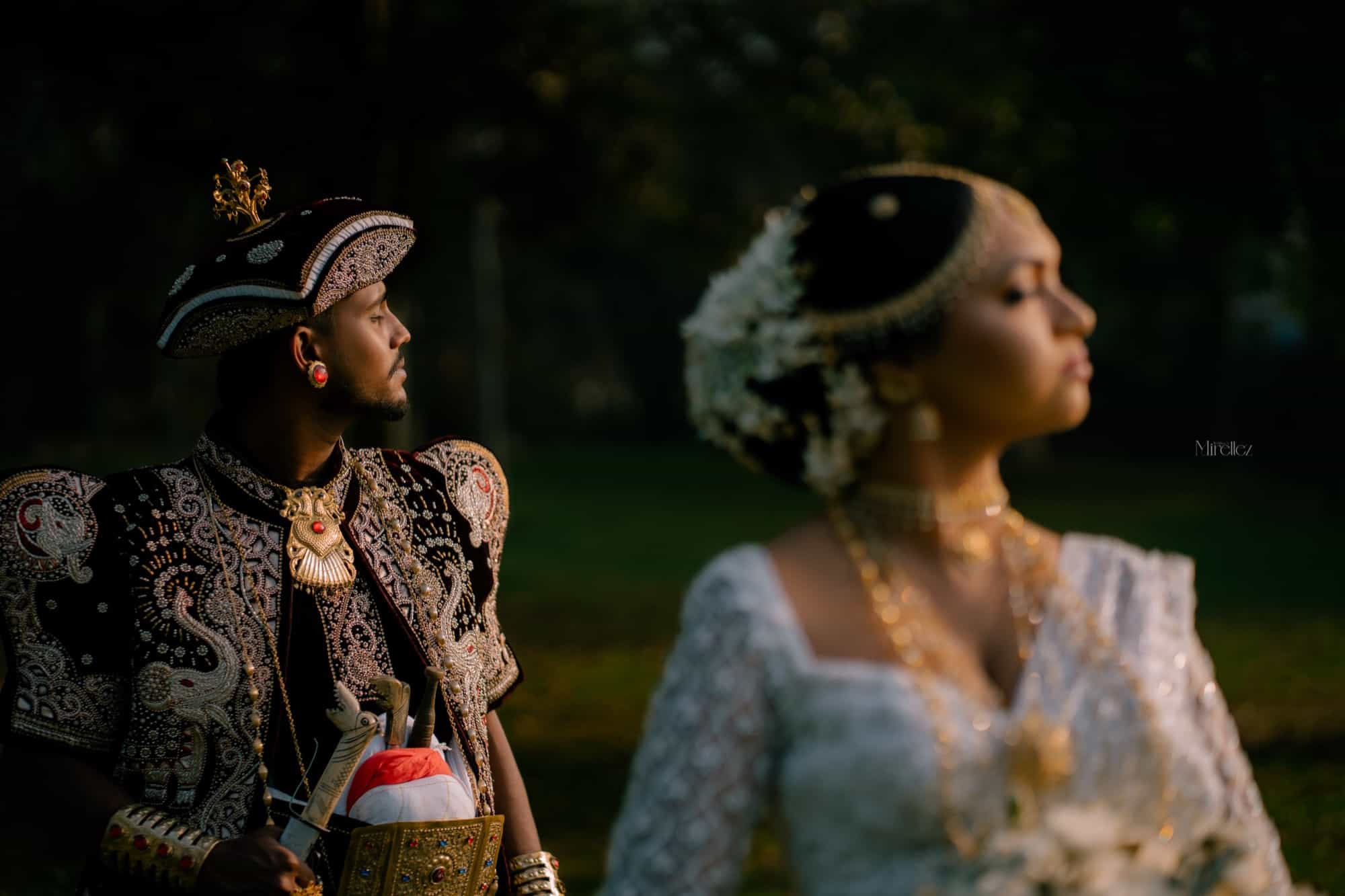 Cinematic profile of the groom in embroidered Kandyan dress looking to the light, the bride's pearl headdress soft in the foreground