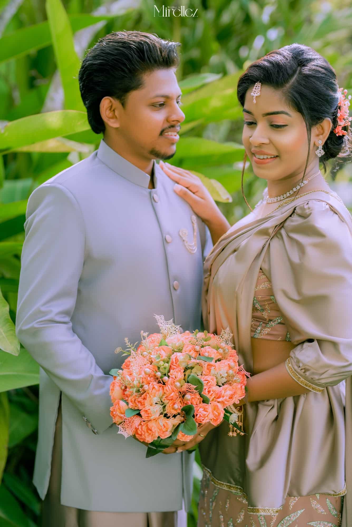Close portrait of the couple among tropical banana leaves, her hand resting on his grey nehru jacket