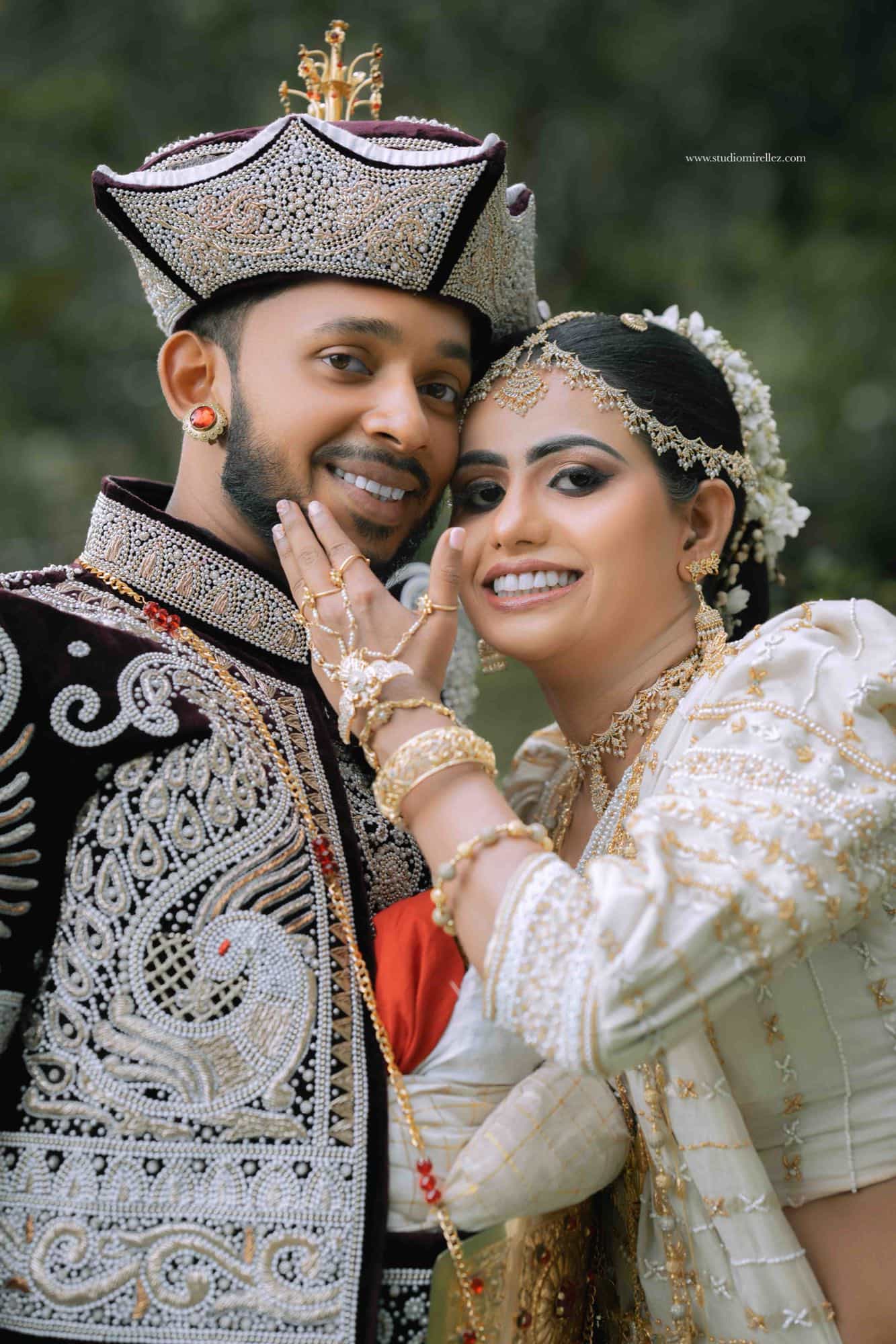 Warm portrait of the couple cheek to cheek, the bride's bangled hand resting at the groom's face, both in white and gold Kandyan dress