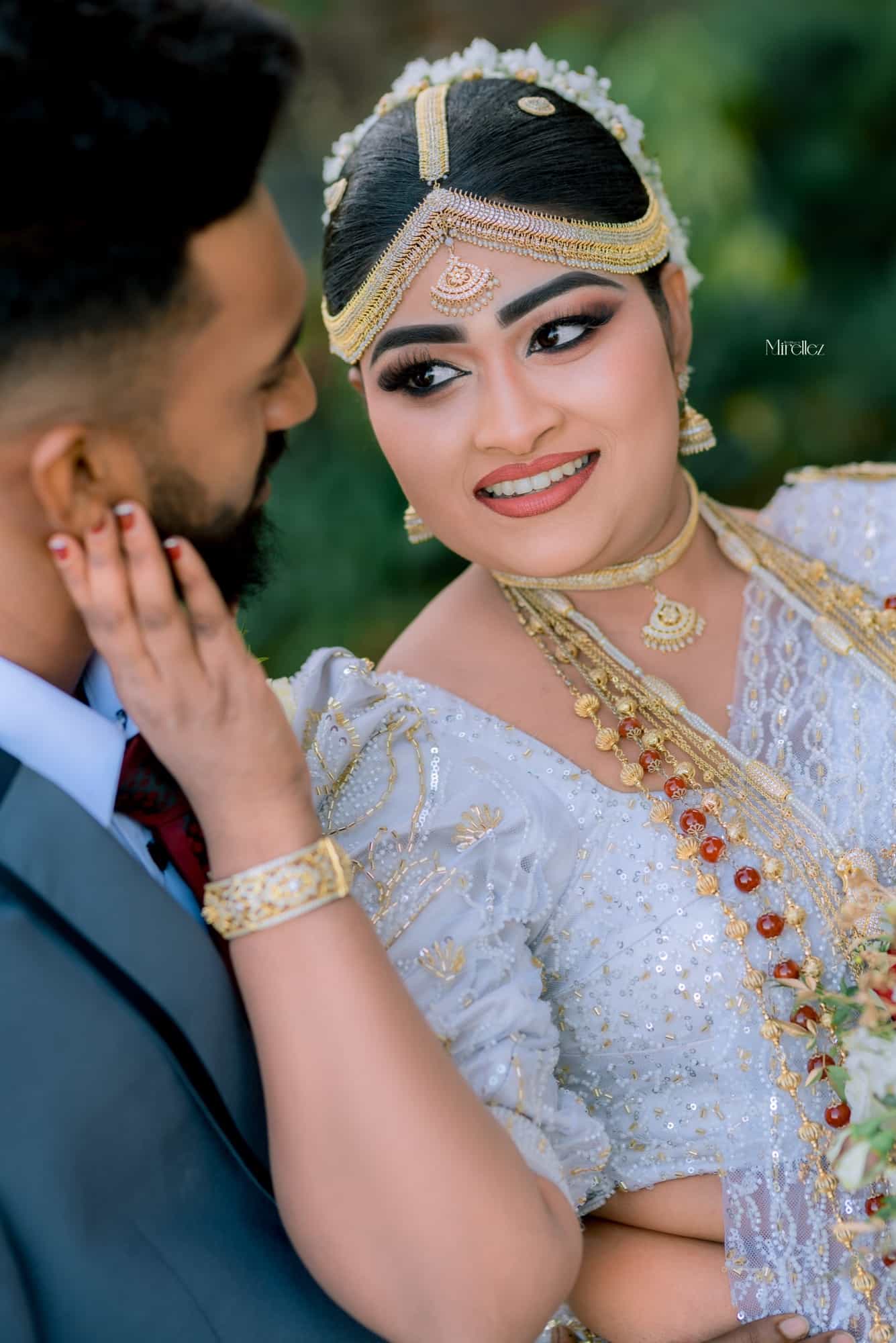 Close portrait of the bride resting her hand on the groom's cheek, her gold headpiece and beaded necklaces catching the light