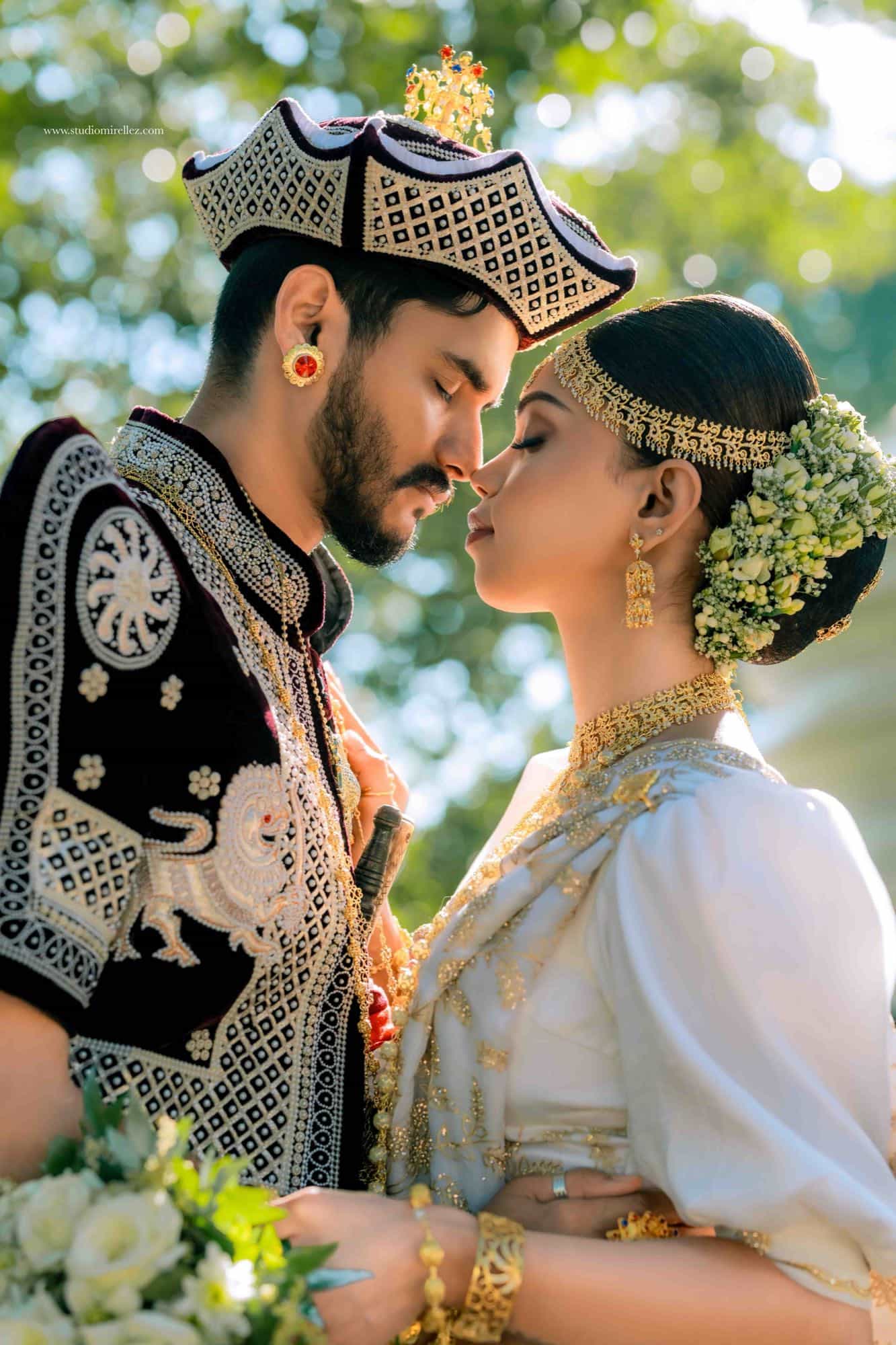 Sunlit close portrait of the bride and groom nose to nose, her layered gold headpiece and jasmine strands glowing