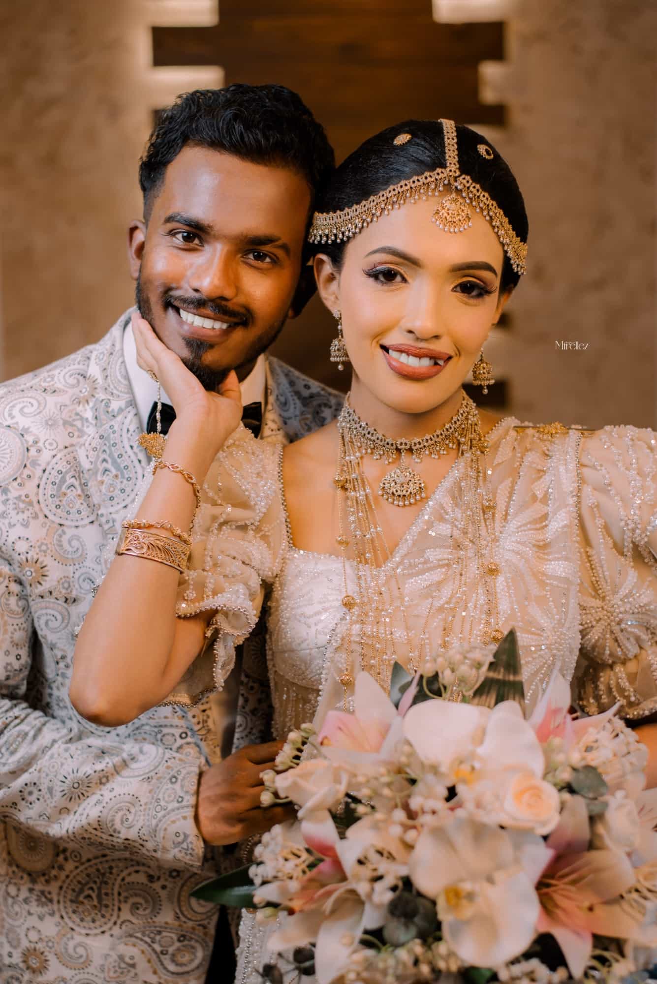Close portrait of Achini and Shiran cheek to cheek, her hand against his chin, in gold headpiece and pearl-beaded Kandyan saree