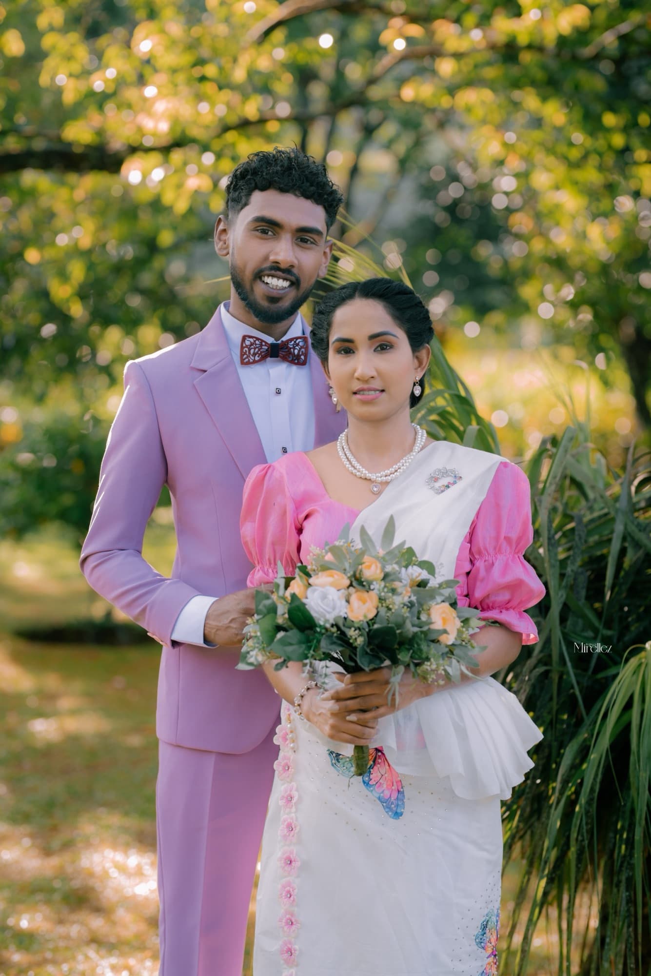 Half-body portrait of the couple facing the camera, the bride holding a rose bouquet against greenery