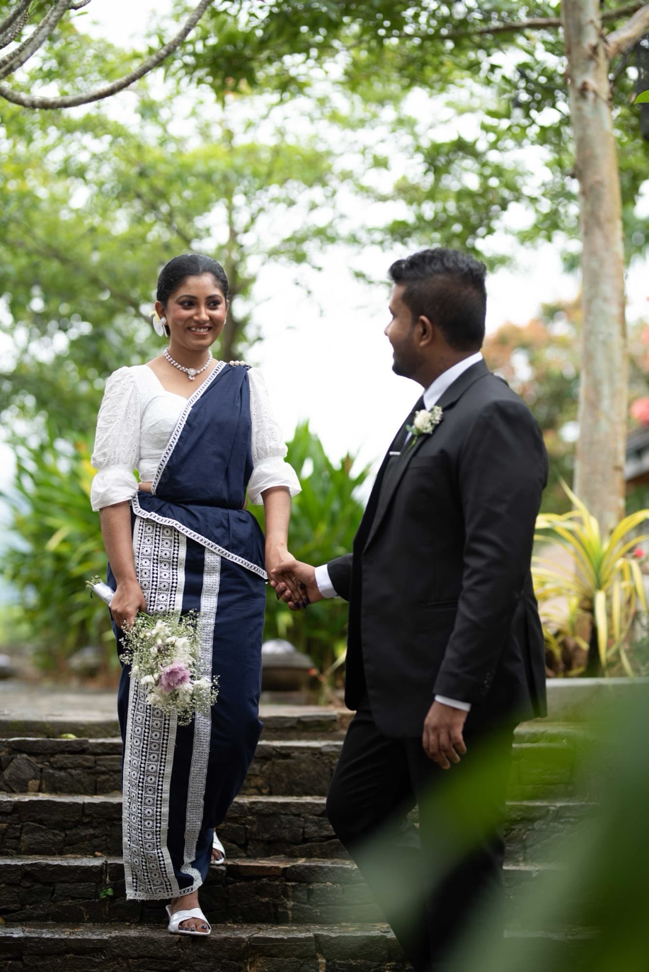 Bride descending stone garden steps hand in hand with the groom, both smiling, surrounded by greenery