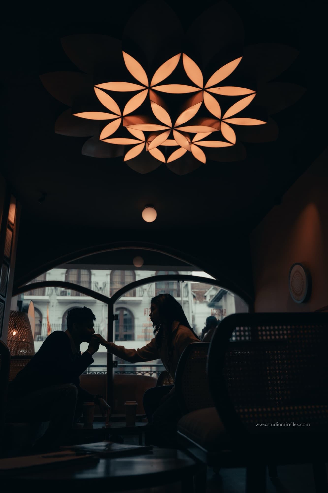 Cinematic silhouette of the couple sharing a tender moment beneath an illuminated floral ceiling light