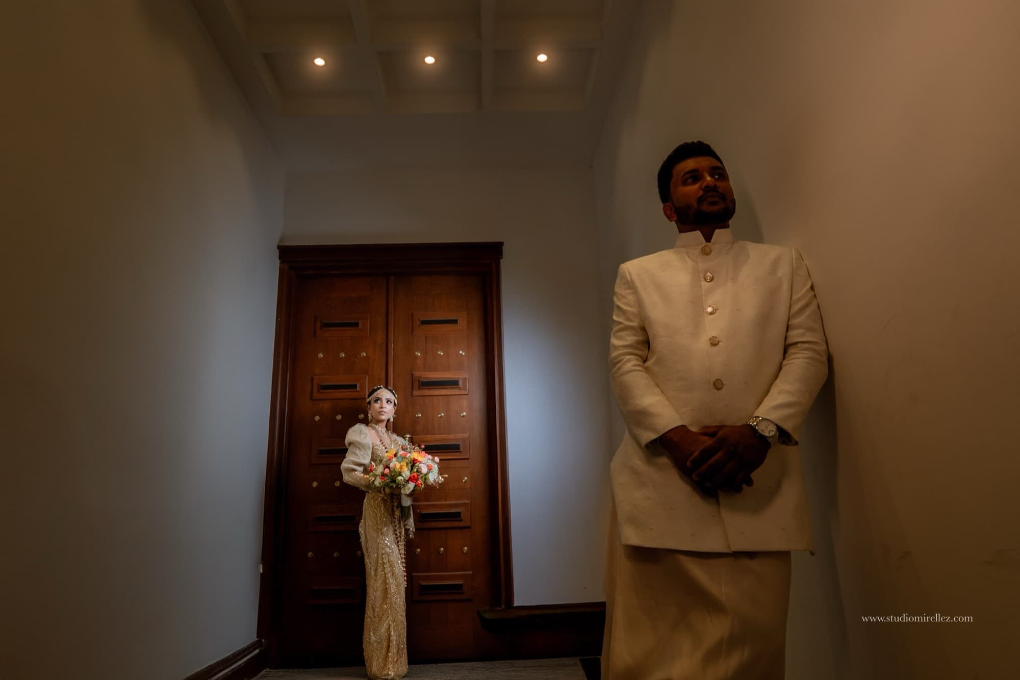 A bride with a bouquet and a groom in cream attire in a moody architectural portrait