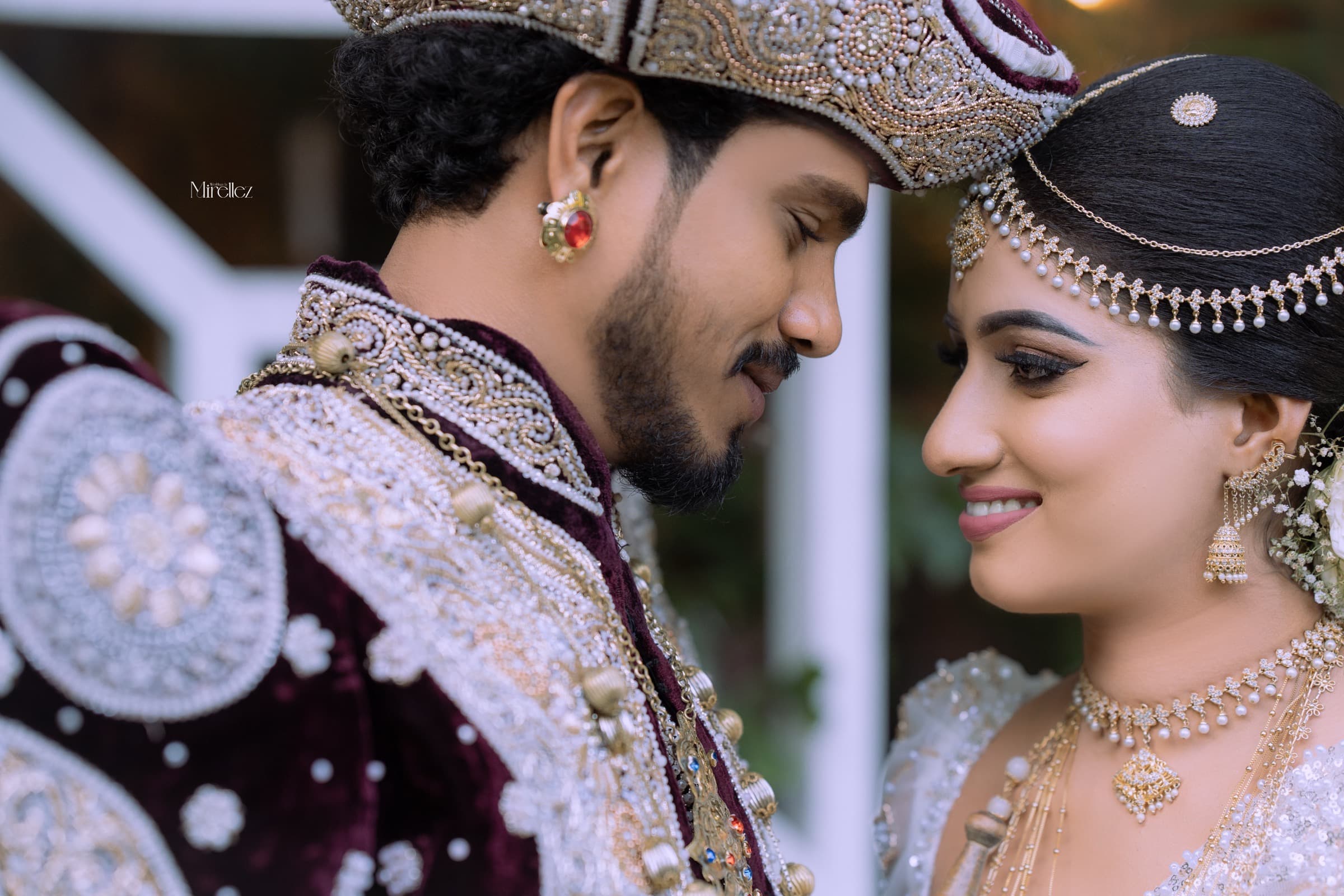 A Kandyan groom and bride forehead to forehead in ornate traditional attire